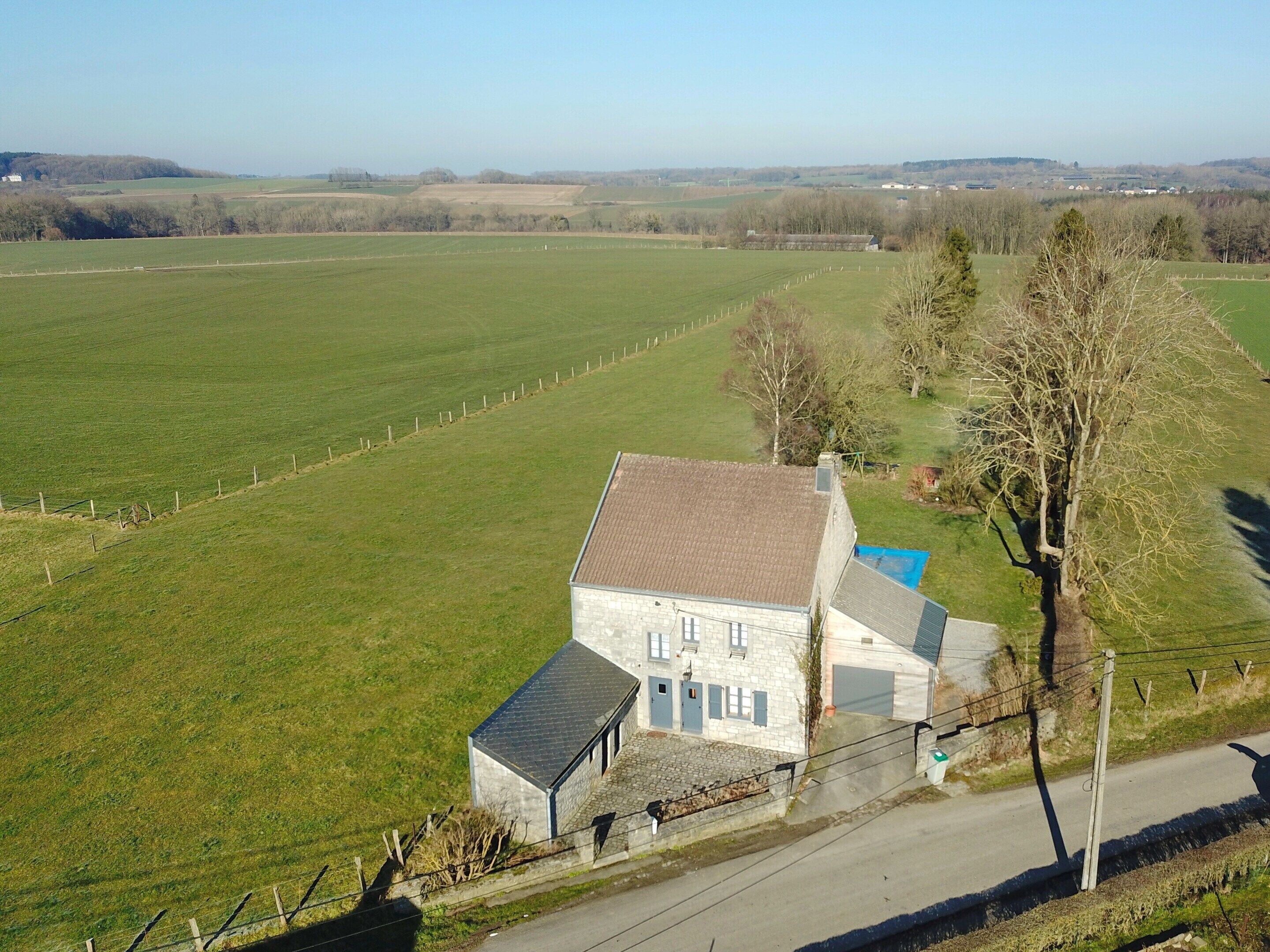 A rural house with a stone facade, a small attached garage, and a fenced field in the background.