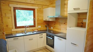 A compact kitchen with wooden walls, a window, a sink, a stove, and white cabinets. - Chalet in Oignies With BBQ and Terrace (Viroinval)