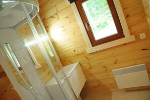 A wooden cabin interior with a window, a white heater, and a glass shower enclosure. - Chalet in Oignies With BBQ and Terrace (Viroinval)