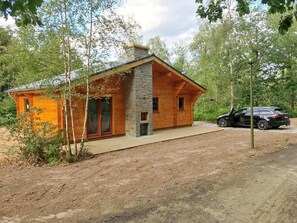 En rustik stuga med en skorsten av sten, träväggar och en bil parkerad utanför.