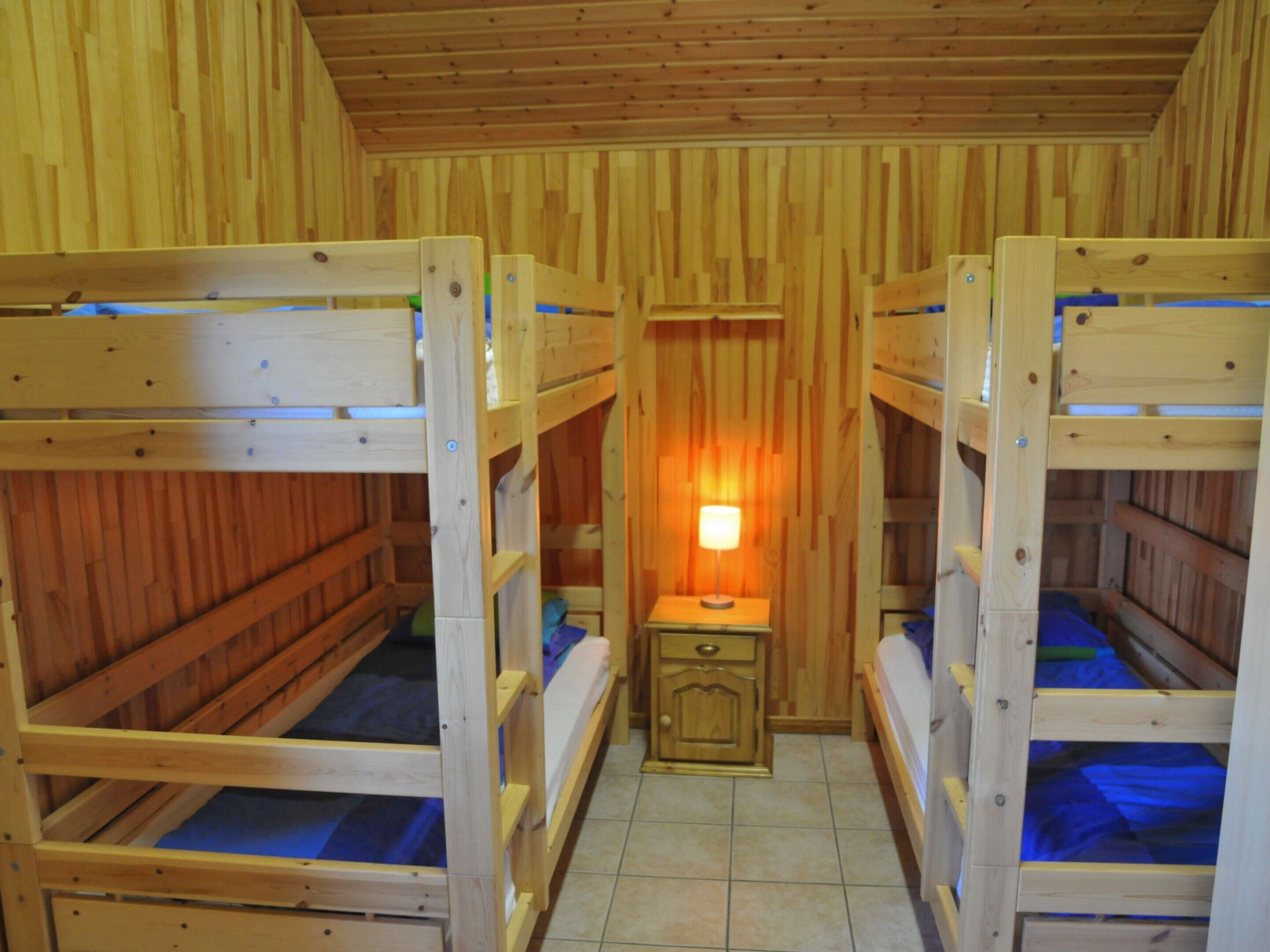 A wooden cabin with bunk beds, a small wooden cabinet, and a lit lamp.