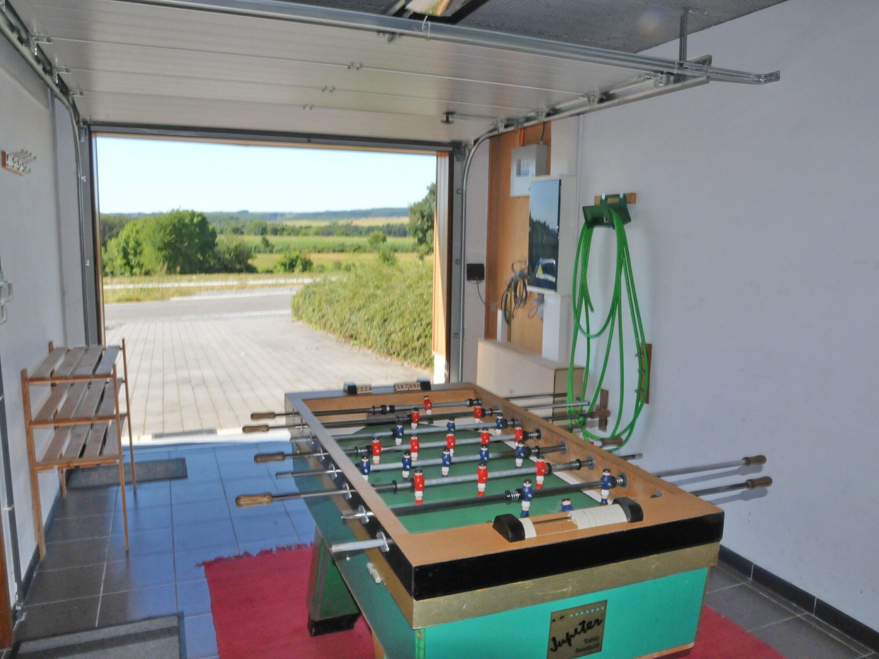 A foosball table in a room with a view of a rural landscape through an open door.