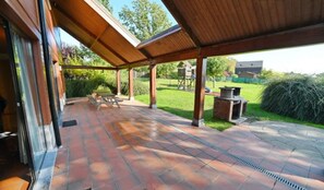 Un patio couvert avec un sol en briques, une table en bois et un barbecue.
