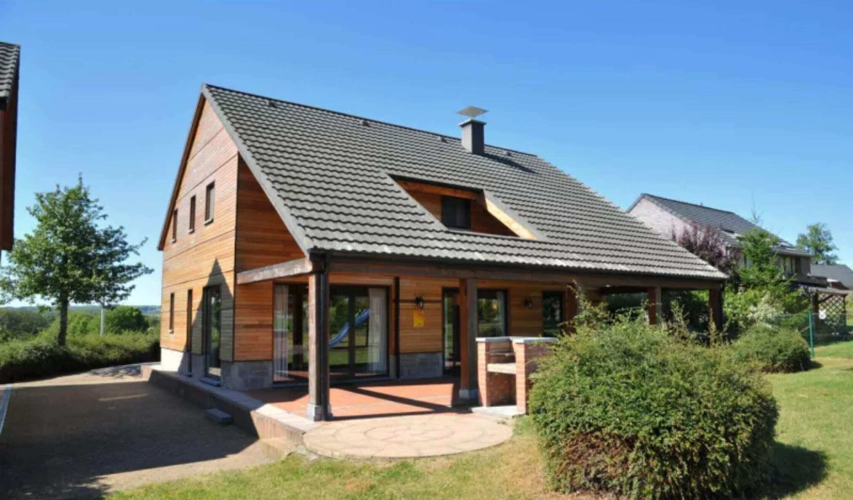 Une maison en bois à deux étages, avec un toit en pente, une cheminée et une véranda couverte.