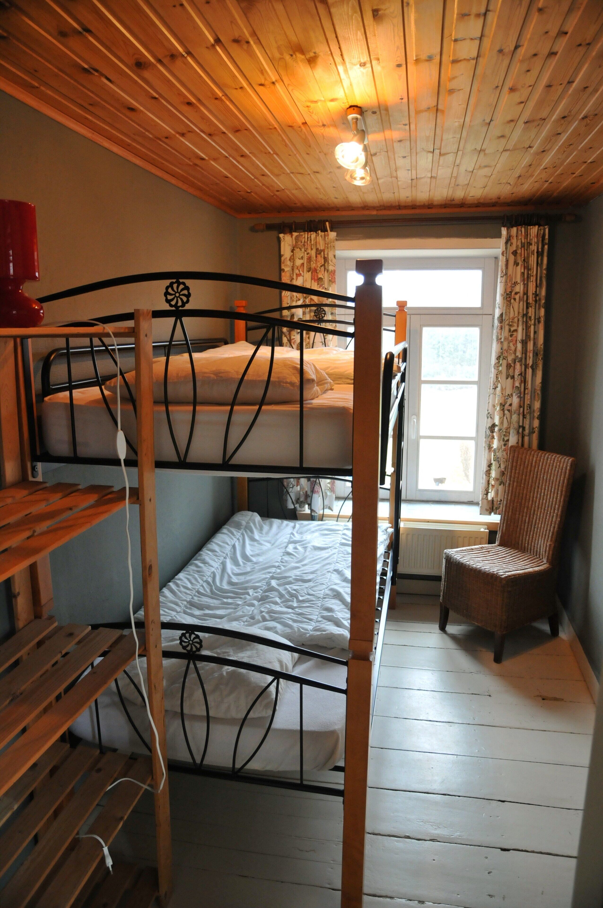 A bunk bed room with wooden floors, a chair, and a window with curtains.
