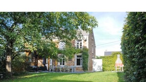 A two-story stone house with a grassy yard, a patio with outdoor furniture, and a chimney. - Holiday Home in Hotton Near Caves of Hotton (Hotton)