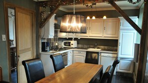 A kitchen with white cabinets, a wooden dining table, and black chairs. - Holiday Home in Hotton Near Caves of Hotton (Hotton)