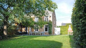 A two-story stone house with a grassy yard, a patio with outdoor furniture, and a chimney. - Holiday Home in Hotton Near Caves of Hotton (Hotton)