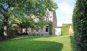 A two-story stone house with a grassy yard, a patio with outdoor furniture, and a chimney. - Holiday Home in Hotton Near Caves of Hotton (Hotton)