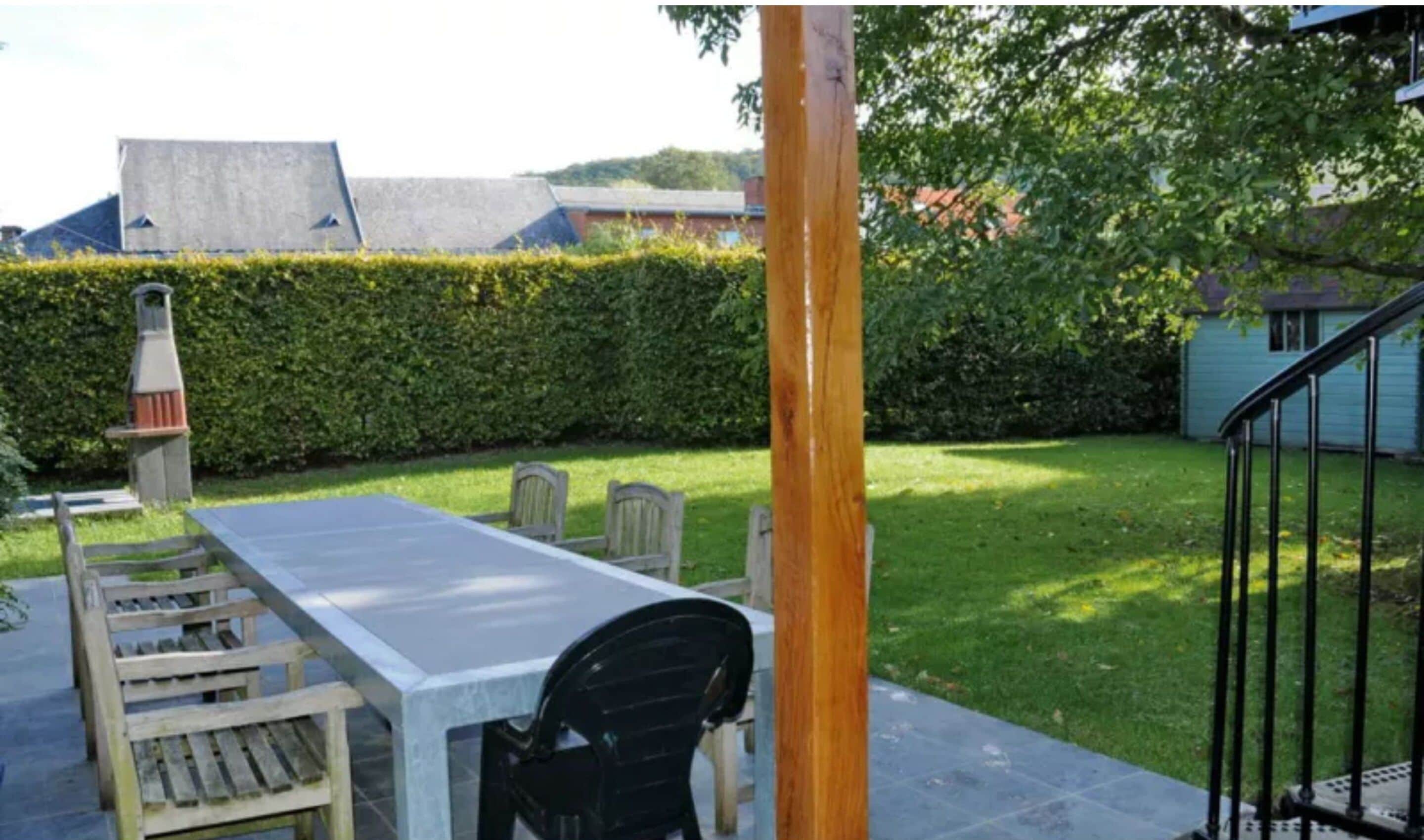An outdoor patio with a table and chairs, a wooden post, and a metal railing.
