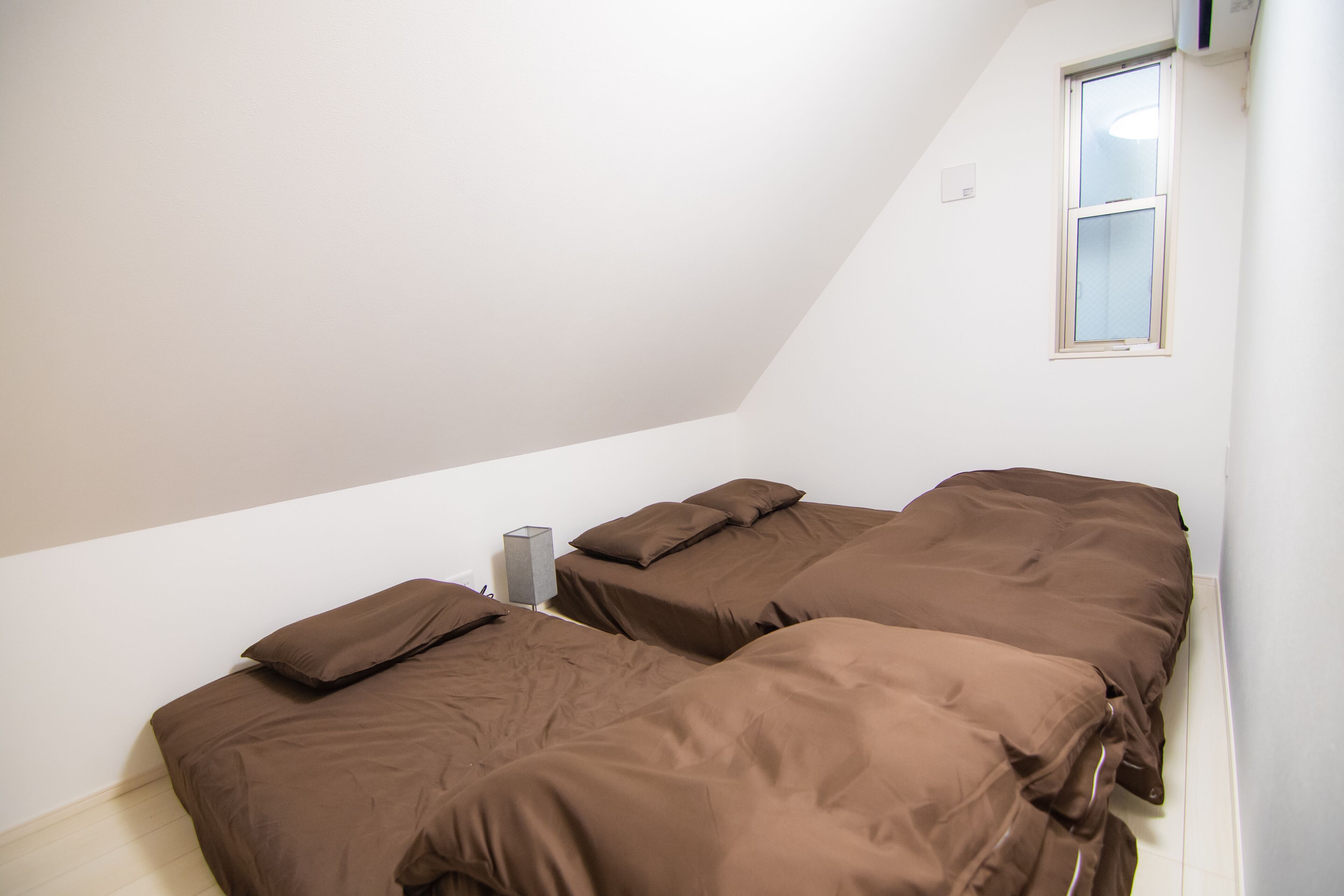 A small, dimly lit room with two beds, a single window, and a small heater.