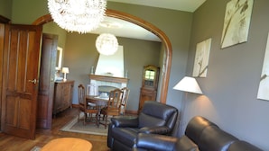 A living room with a leather sofa, wooden coffee table, and a dining area with a chandelier. - Holiday Home in Durbuy With Garden & BBQ (Durbuy)