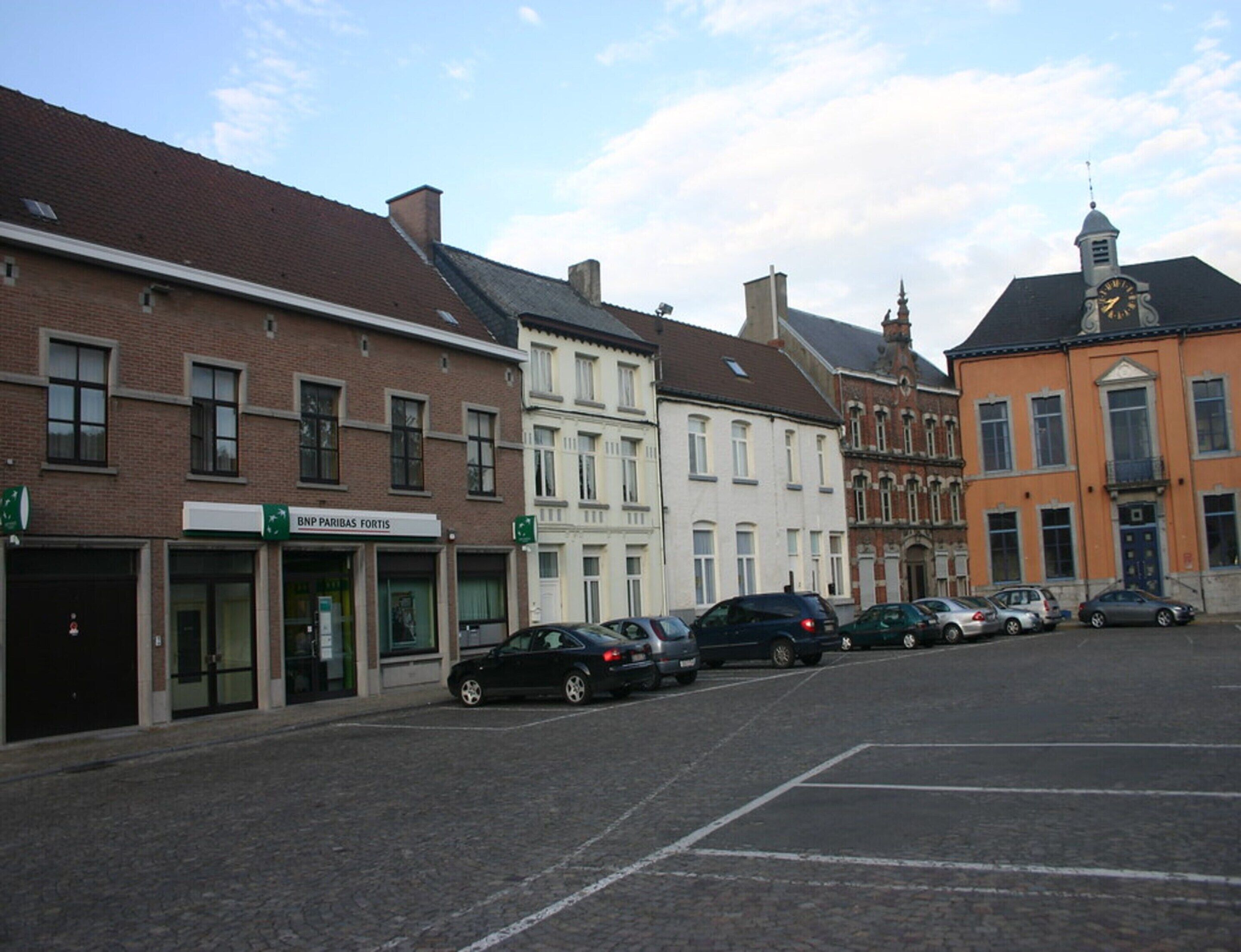 Une rue bordée de voitures garées et d’immeubles abritant des commerces.