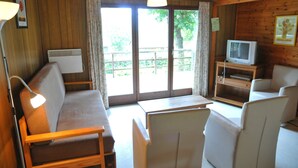 Ein Zimmer mit Holzvertäfelung, einer Couch, einem Tisch, einem Fernseher und Blick durch Glastüren.