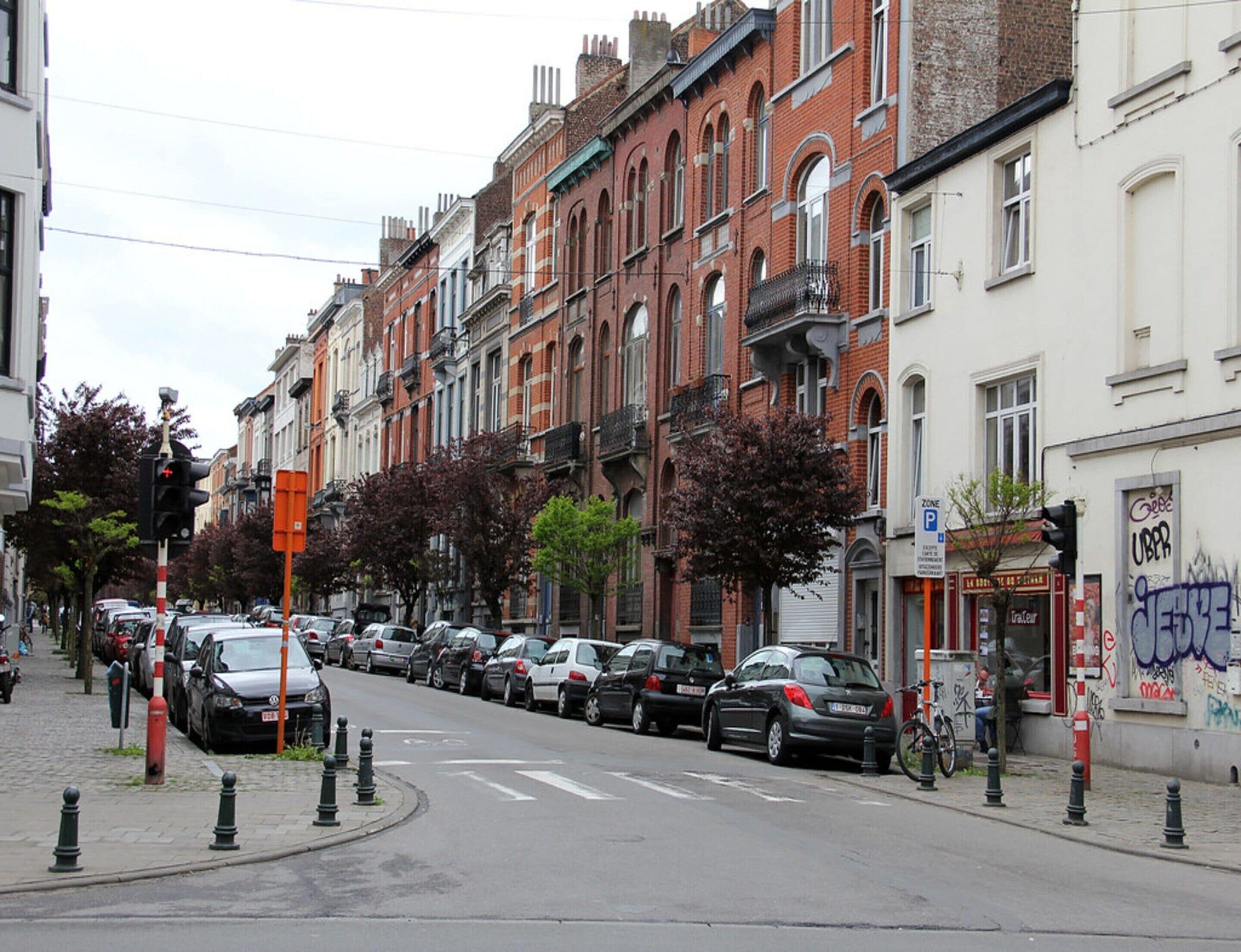 A street lined with parked cars and buildings, including a visible storefront with a sign.