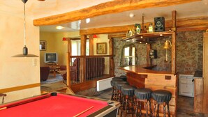 Ein Billardtisch mit roter Spielvliesbahn, ein Barbereich mit Hockern und ein Fernseher im Hintergrund.