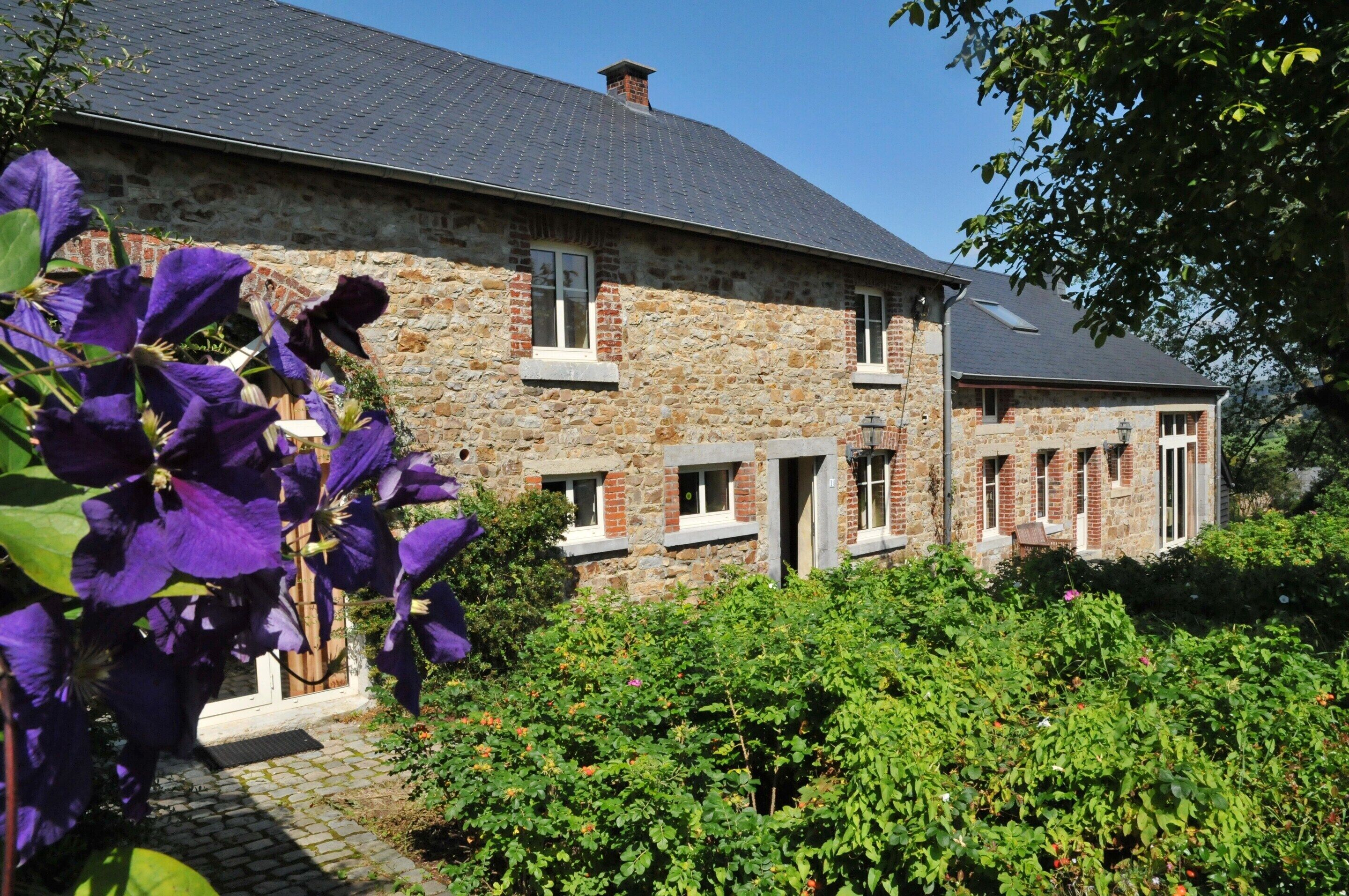 Un bâtiment en pierre avec un toit en pente, une cheminée en briques et un petit porche.