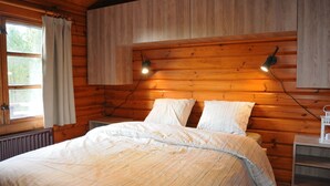 Ett sovrum i en stuga med träpanel, en säng, två sänglampor och ett fönster med gardiner.