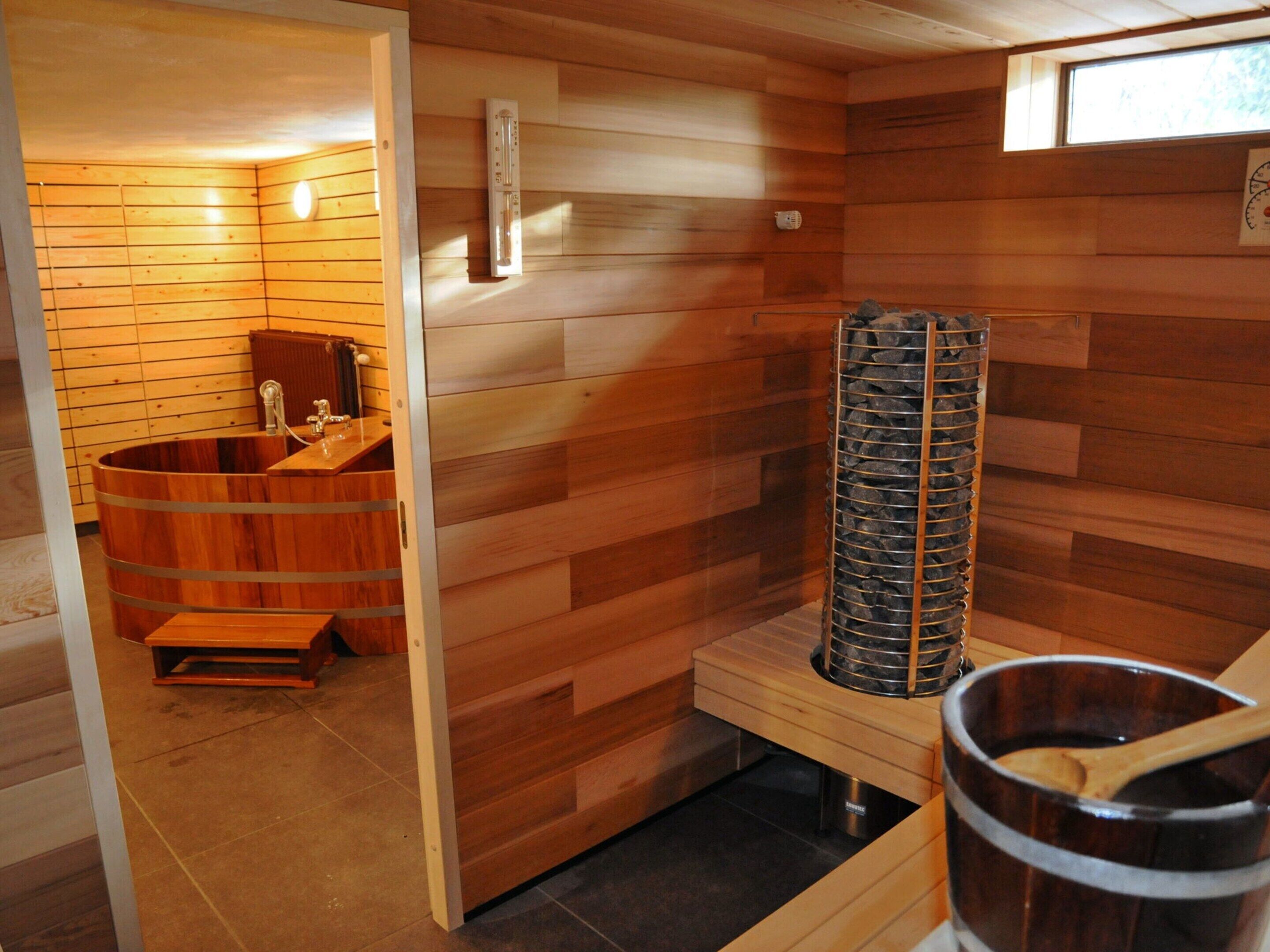 Una sauna amb parets de fusta, una banyera de fusta, un escalfador de sauna i una paret de pedra.