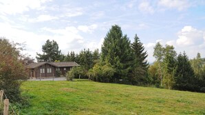 En enkel stuga med ett sluttande tak, omgiven av en gräsklädd äng och en tät skog.