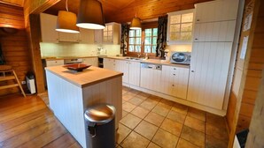 A wooden cabin kitchen with a central island, white cabinets, and pendant lighting. - Holiday Home in Durbuy With Garden (Durbuy)