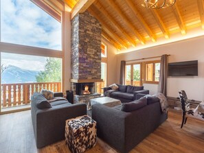 A cozy living room with a stone fireplace, wooden beams, and a view of mountains. - Chalet in Riddes Near Ski Lift Les 4 Vallees (Riddes)