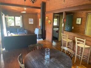 A wooden interior with a round table, chairs, a sofa, and a grill.