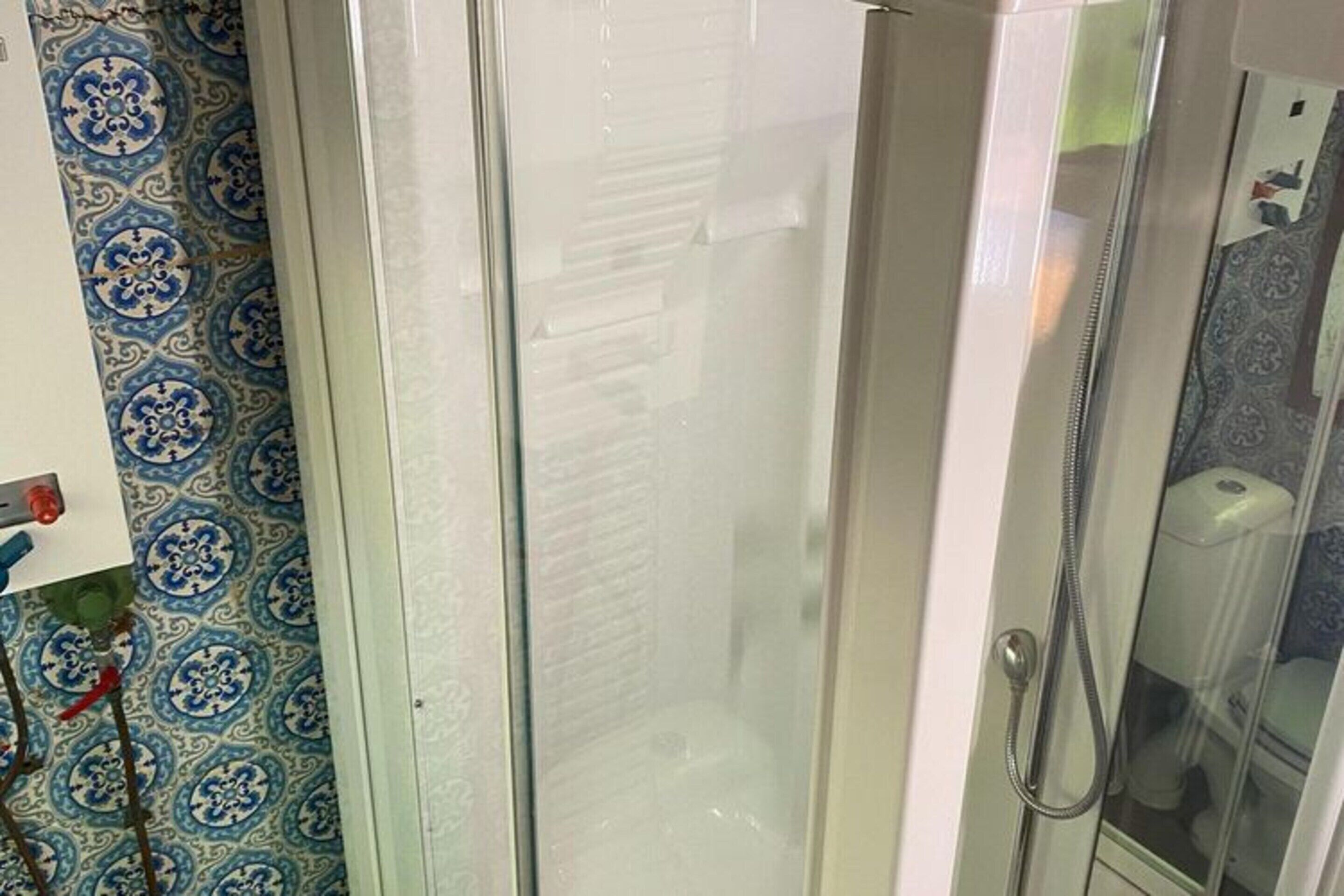 A glass-enclosed shower stall with a showerhead and a handheld shower attachment.