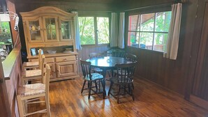 A dining area with a wooden table and chairs, a cabinet with glass doors, and large windows with curtains. - Ortho Hideaway With Garden (La Roche-en-Ardenne)