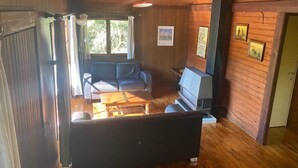 A cozy cabin interior with a sofa, a small table, a fireplace, and wooden walls. - Ortho Hideaway With Garden (La Roche-en-Ardenne)