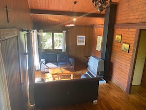 A cozy cabin interior with a sofa, a small table, a fireplace, and wooden walls.