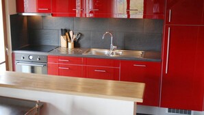 A modern kitchen with red cabinets, a stainless steel stove, and a double sink. - Chalet for 6 People With Views of Veysonnaz (Veysonnaz)