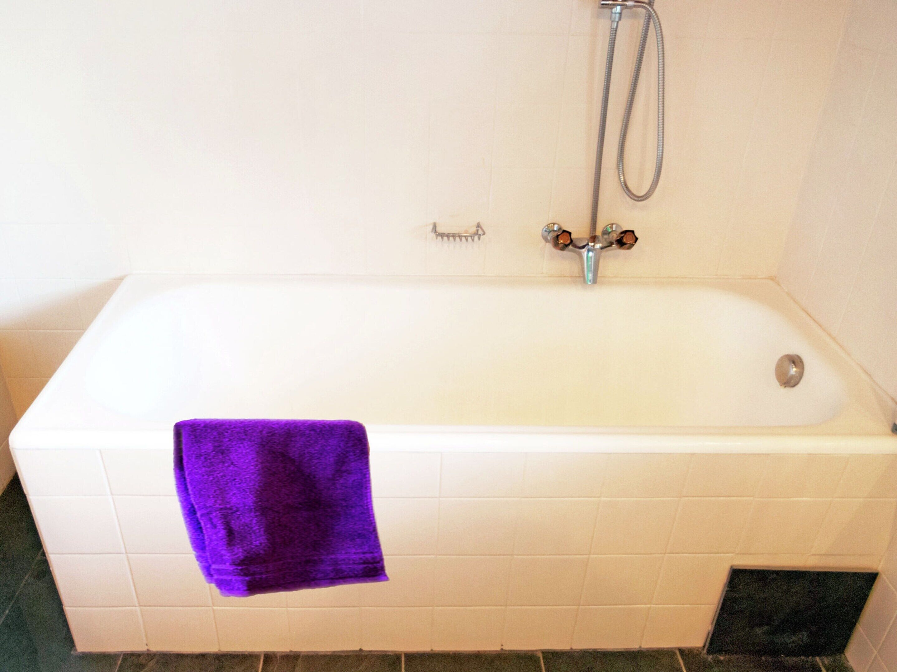 A standard white bathtub with a purple towel, a showerhead, and a small shelf.