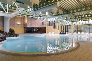 Ein Innenpool mit klarem Wasser, umgeben von Liegestühlen und einem gefliesten Boden.