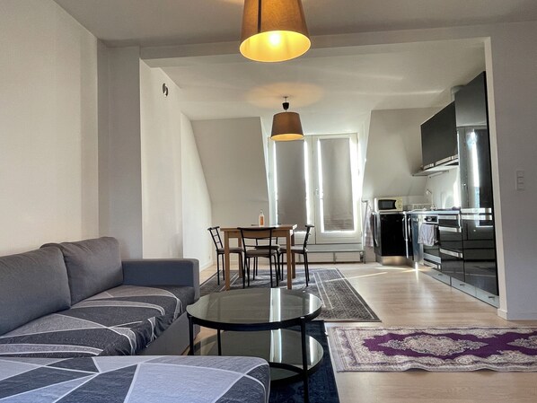 Un salon moderne avec un canapé, une table basse en verre et un coin repas avec des chaises.