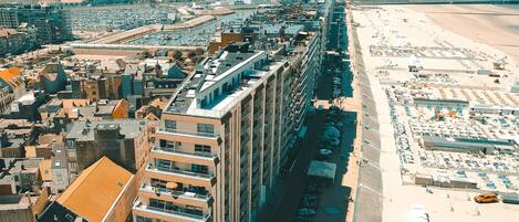 Un hotel de gran altura con varios balcones, ubicación frente a la playa y un puerto deportivo al fondo.