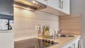A modern kitchen with a built-in stove, stainless steel sink, and wooden cabinetry. - Comfortable Studio With a View Over the City (Blankenberge)