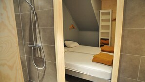 Una camera compatta con doccia, un letto e un piccolo armadio in legno.