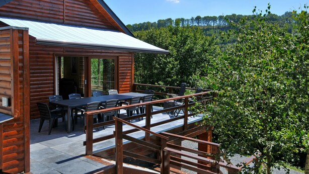 Una baita in legno con un patio, posti a sedere all'aperto e vista su una collina boscosa.