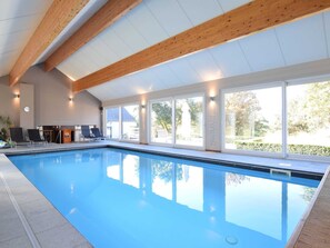 Ein Hallenbad mit klarem, blauem Wasser, Holzbalken an der Decke und großen Fenstern mit Blick ins Freie.