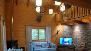 A cozy log cabin interior with a sofa, ottoman, stone wall, television, and a deer head mounted on the wall. - Spacious Chalet Located at Bomal with Hot Tub & Garden Parlour (Durbuy)