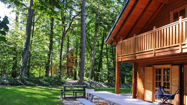 A wooden cabin with a deck, picnic tables, and a stroller. - Spacious Chalet Located at Bomal with Hot Tub & Garden Parlour (Durbuy)