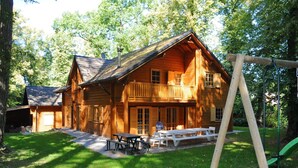 A wooden cabin with a balcony, a picnic table, and a swing set in a wooded area. - Spacious Chalet Located at Bomal with Hot Tub & Garden Parlour (Durbuy)