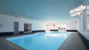 Uma piscina interna com piso azulejado, teto com padrão de grade e porta que dá para o exterior.