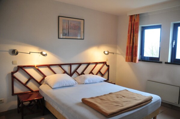 Un letto con testiera in legno, un comodino, una finestra con tende e un quadro appeso al muro.