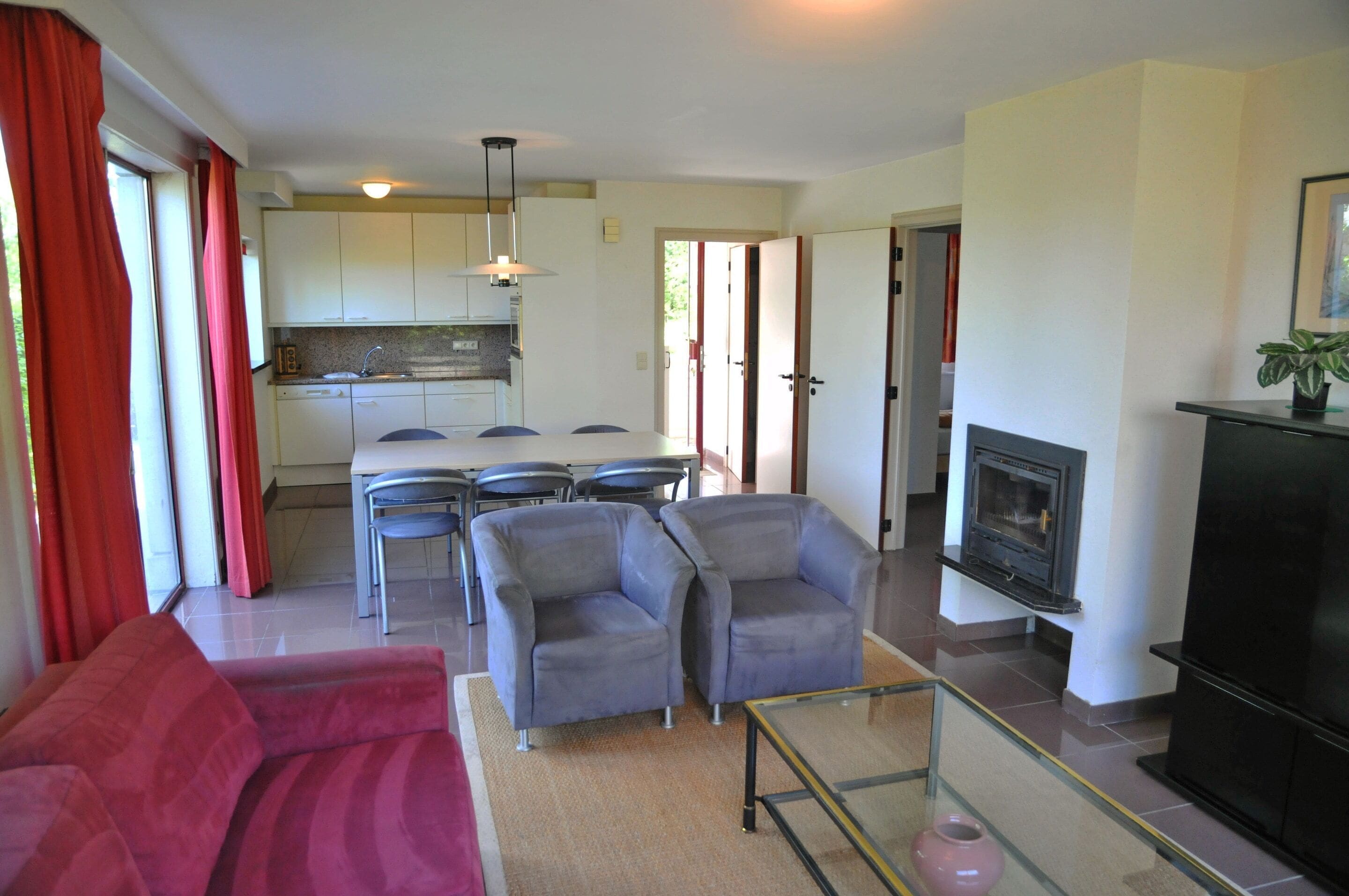 A living room with a red sofa, grey armchairs, a glass coffee table, and a fireplace.