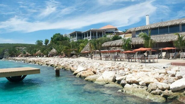 Un hôtel situé en bord de mer, avec une côte rocheuse, une eau turquoise cristalline et des constructions à toits de chaume.