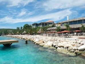 Un hôtel situé en bord de mer, avec une côte rocheuse, une eau turquoise cristalline et des constructions à toits de chaume.