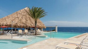 Un espace piscine avec des chaises longues, une structure à toit de chaume et une vue sur l’océan.