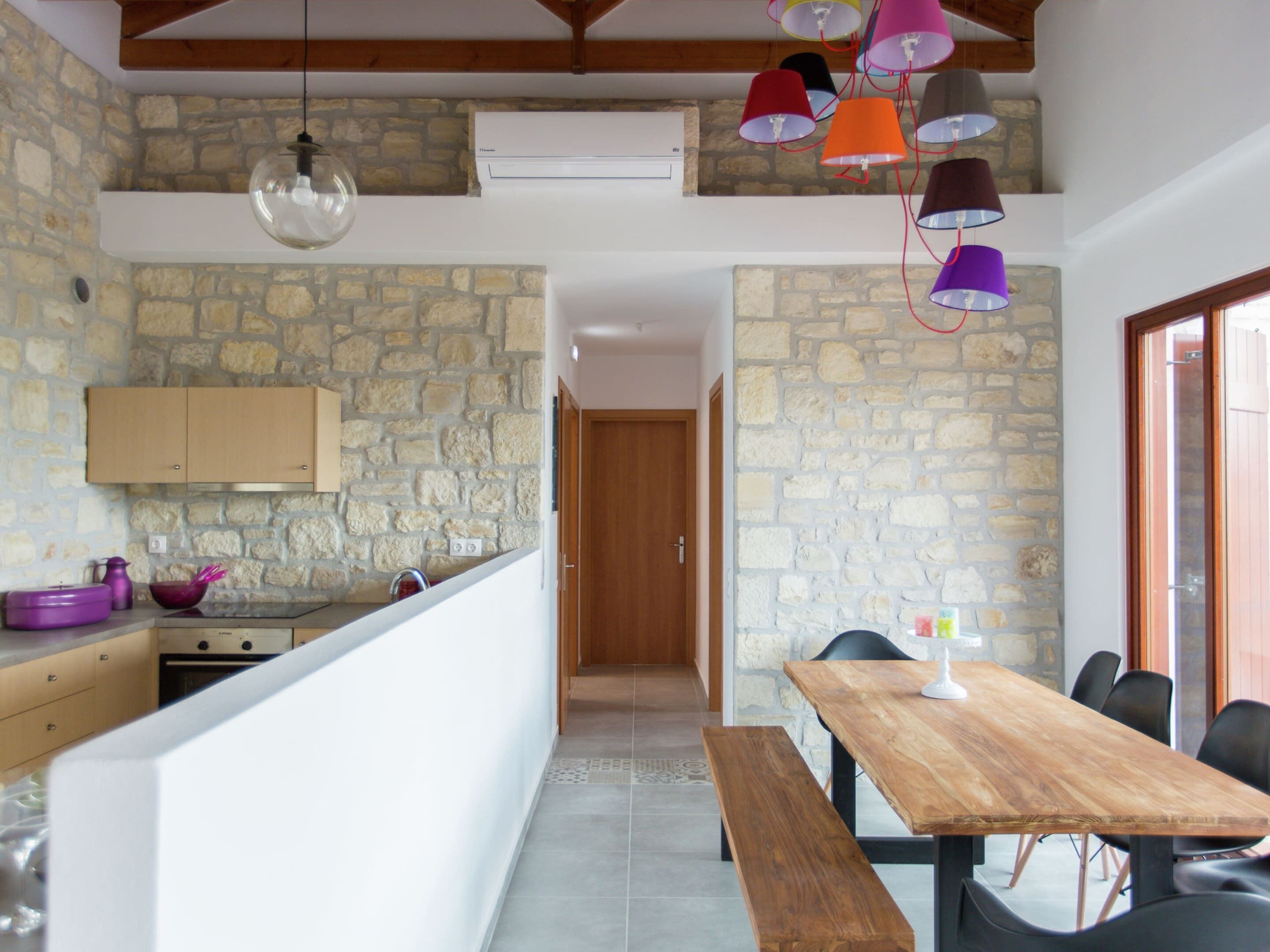 A kitchen with stone walls, wooden beams, and a wooden dining table with chairs.